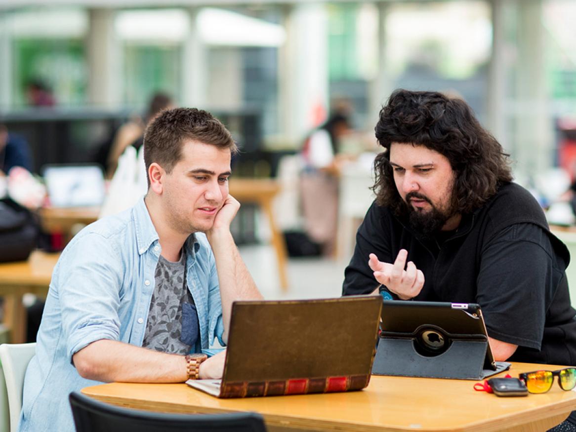 Two students sitting at a table with laptops.