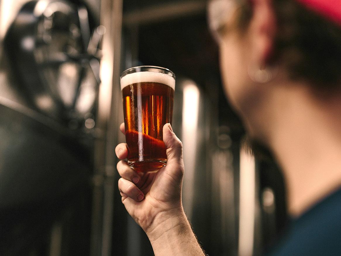 Person holding a glass of beer in a brewery
