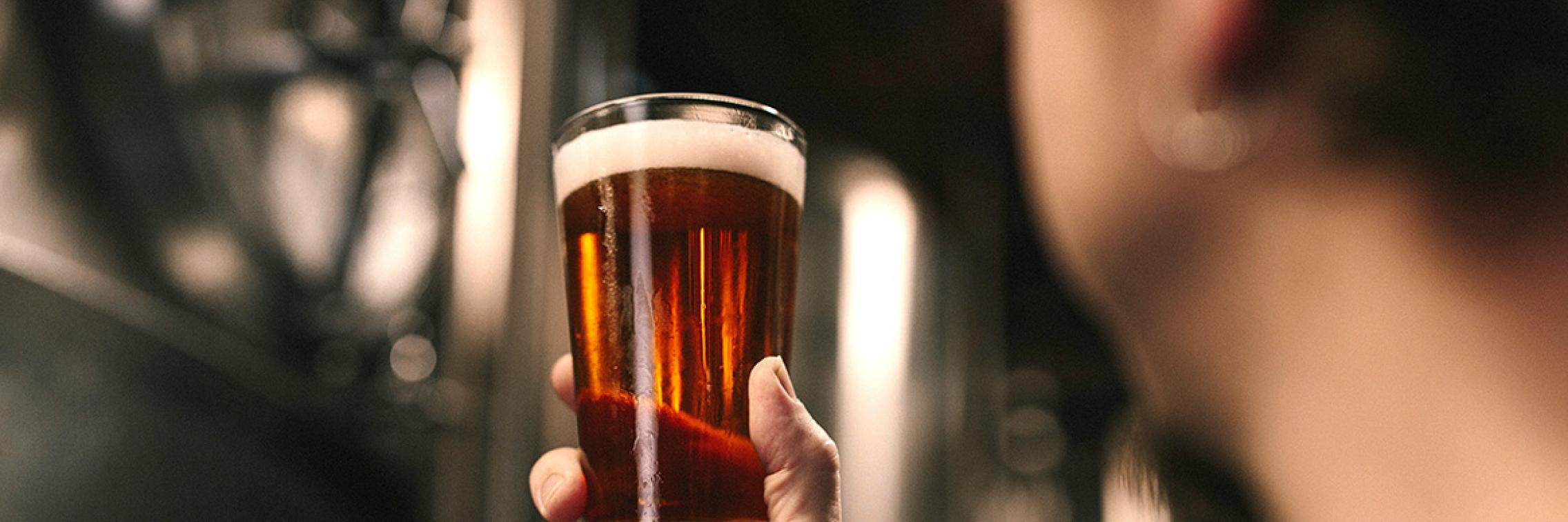 Person holding a glass of beer in a brewery