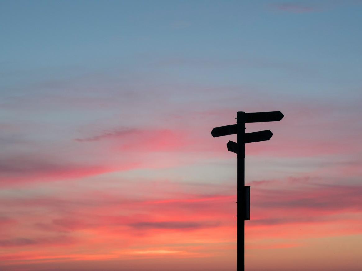 A silhouette of a street sign with arrows pointing in multiple directions at sunset.
