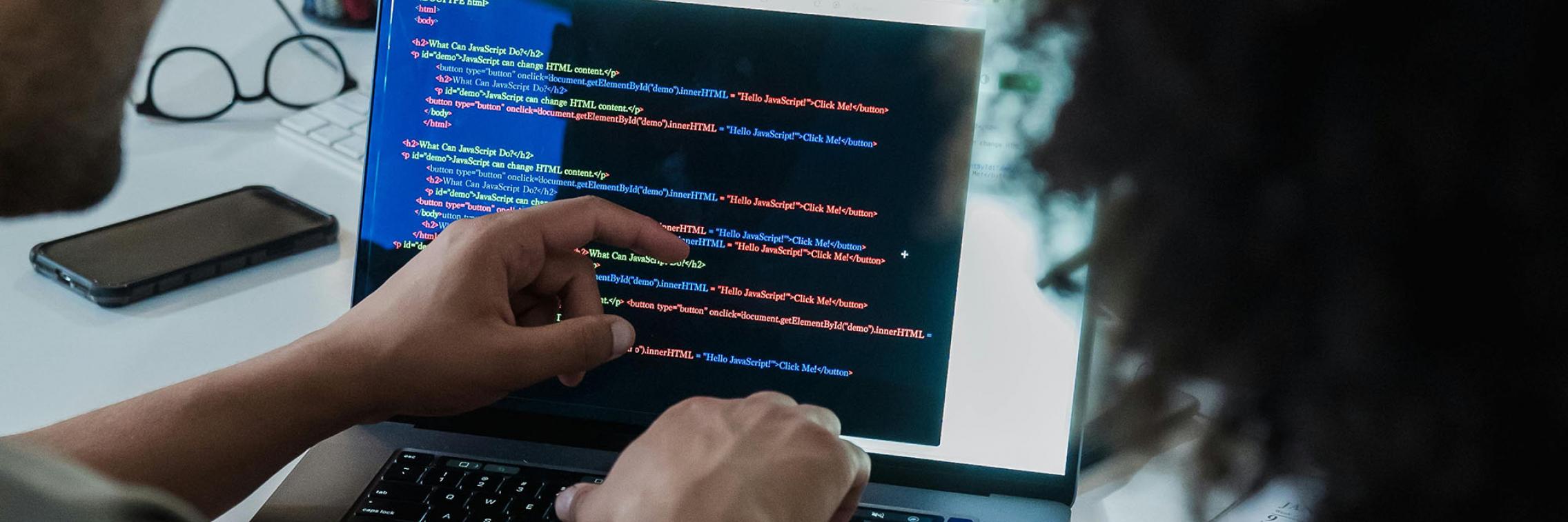 Two people reading HTML code on a laptop screen