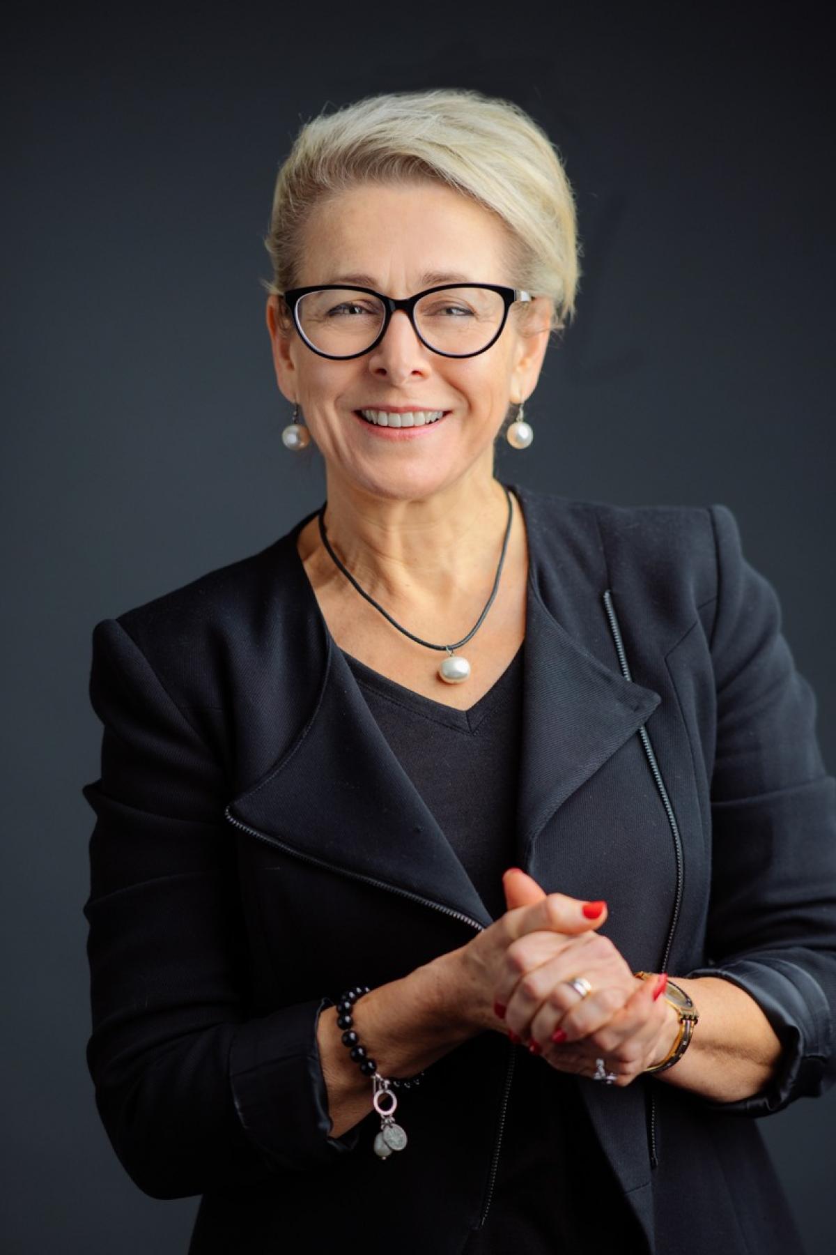Dr Rachel Spencer in a black suit, smiling with hands clasped