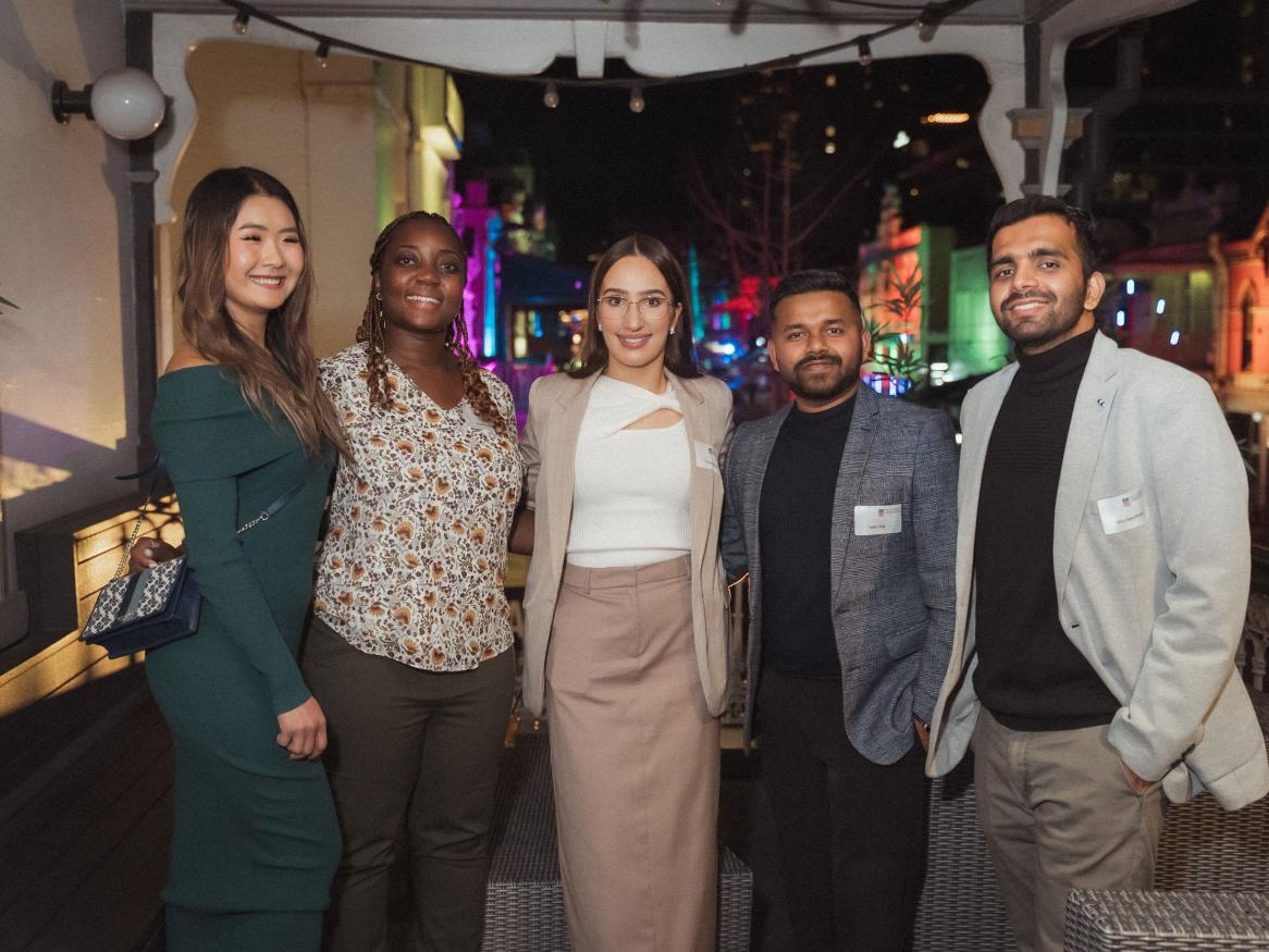 5 alumni members of the YAN committee smiling, at night, with lights behind
